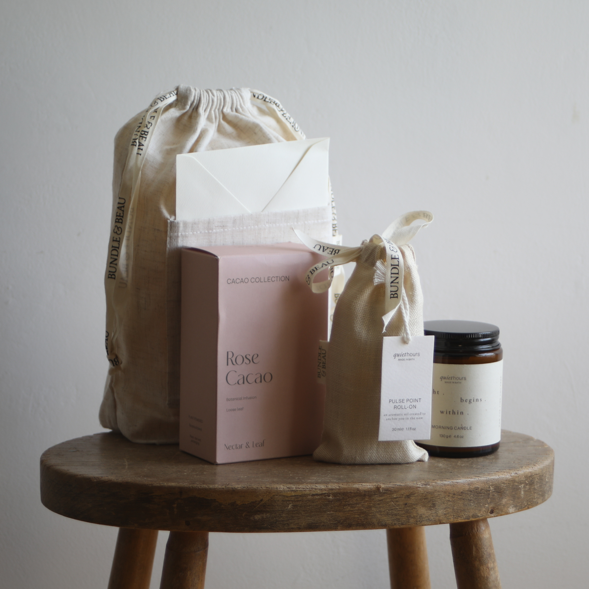 Collection of beauty products including a box labeled 'Rose Cacao', a jar, and a pouch on a wooden stool.