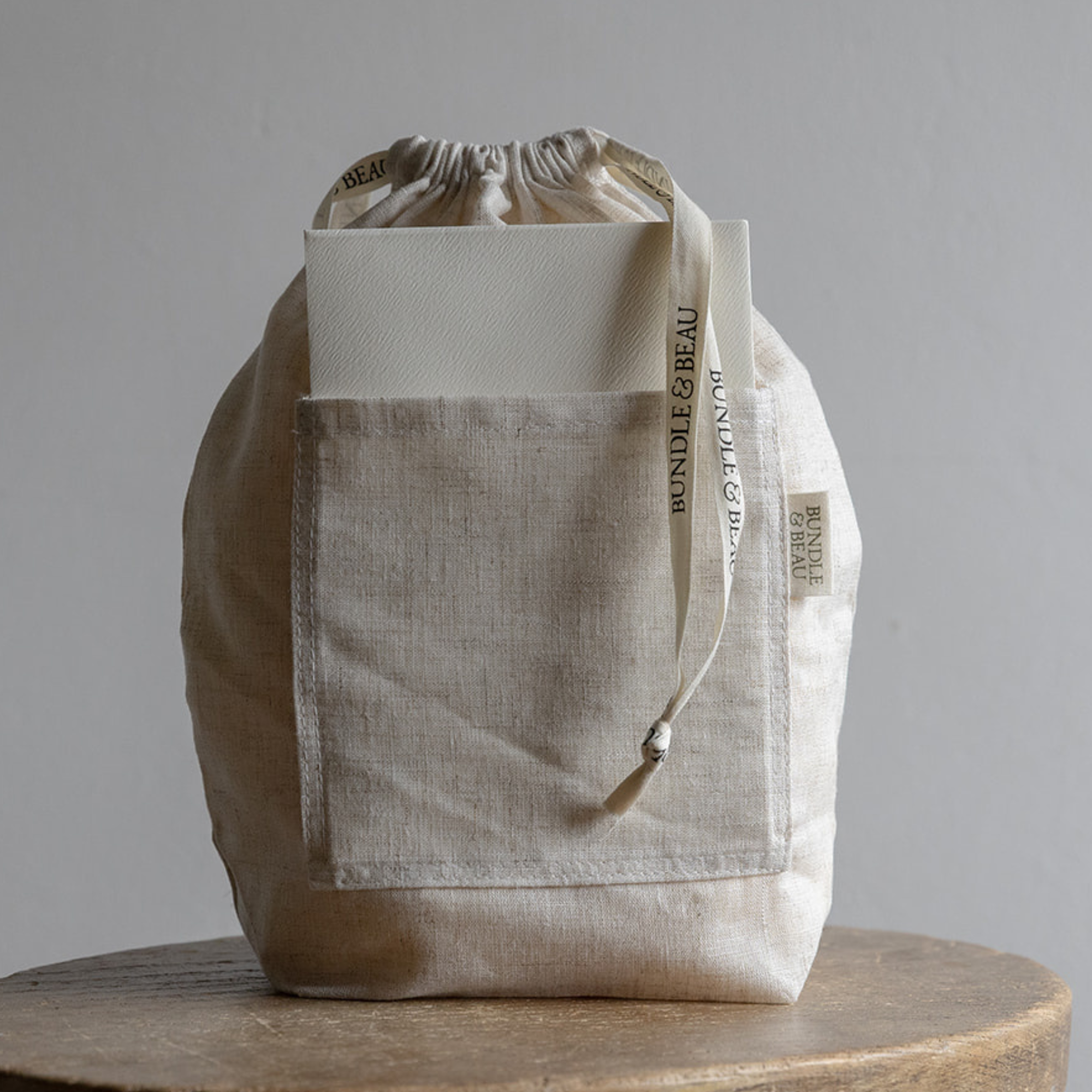 Beige tote bag with drawstring on a wooden surface against a gray background