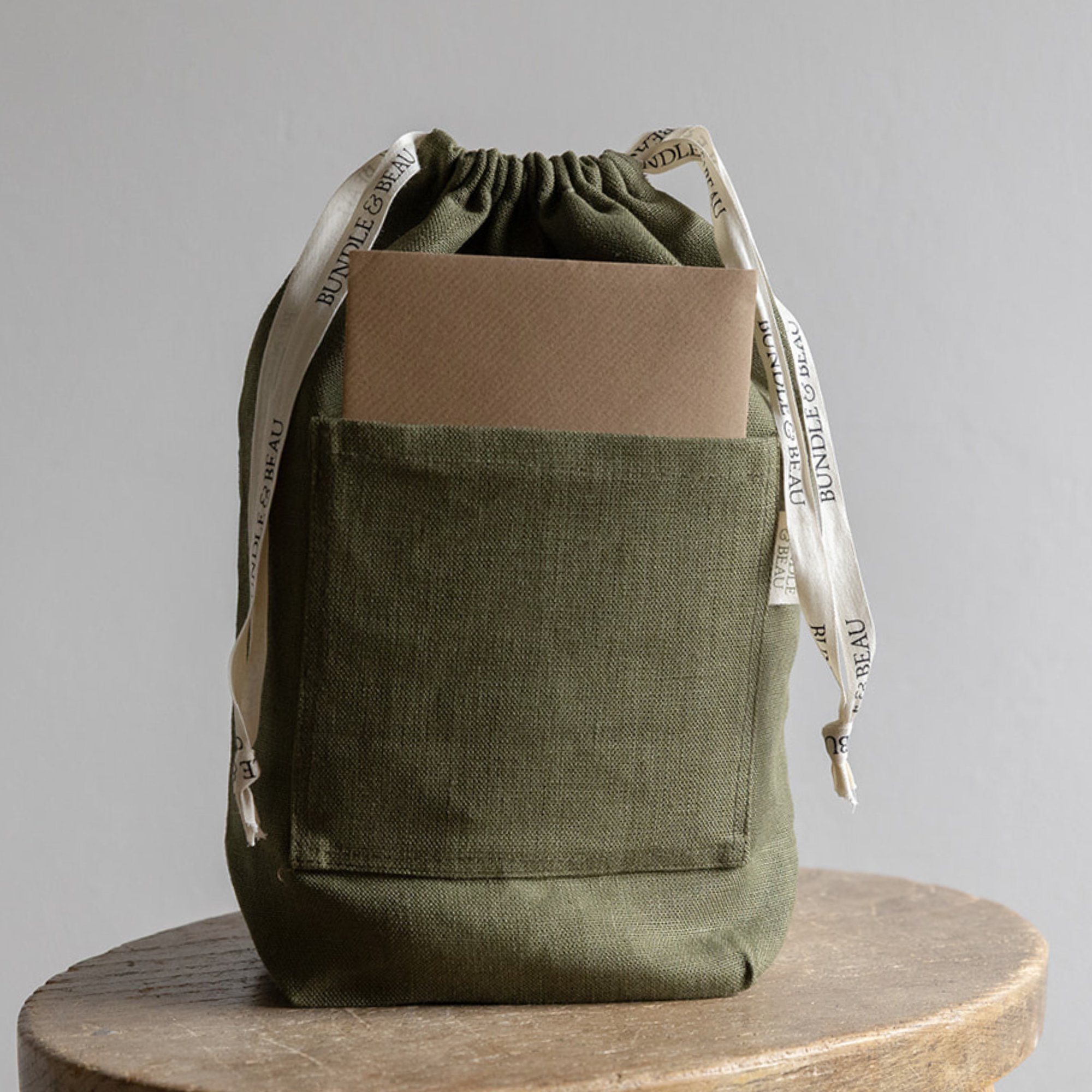 Green drawstring bag with a brown pocket on a wooden surface and gray background