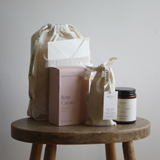 Collection of beauty products including a box labeled 'Rose Cacao', a jar, and a pouch on a wooden stool.