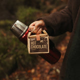 Person holding a container of hot chocolate in a forest setting