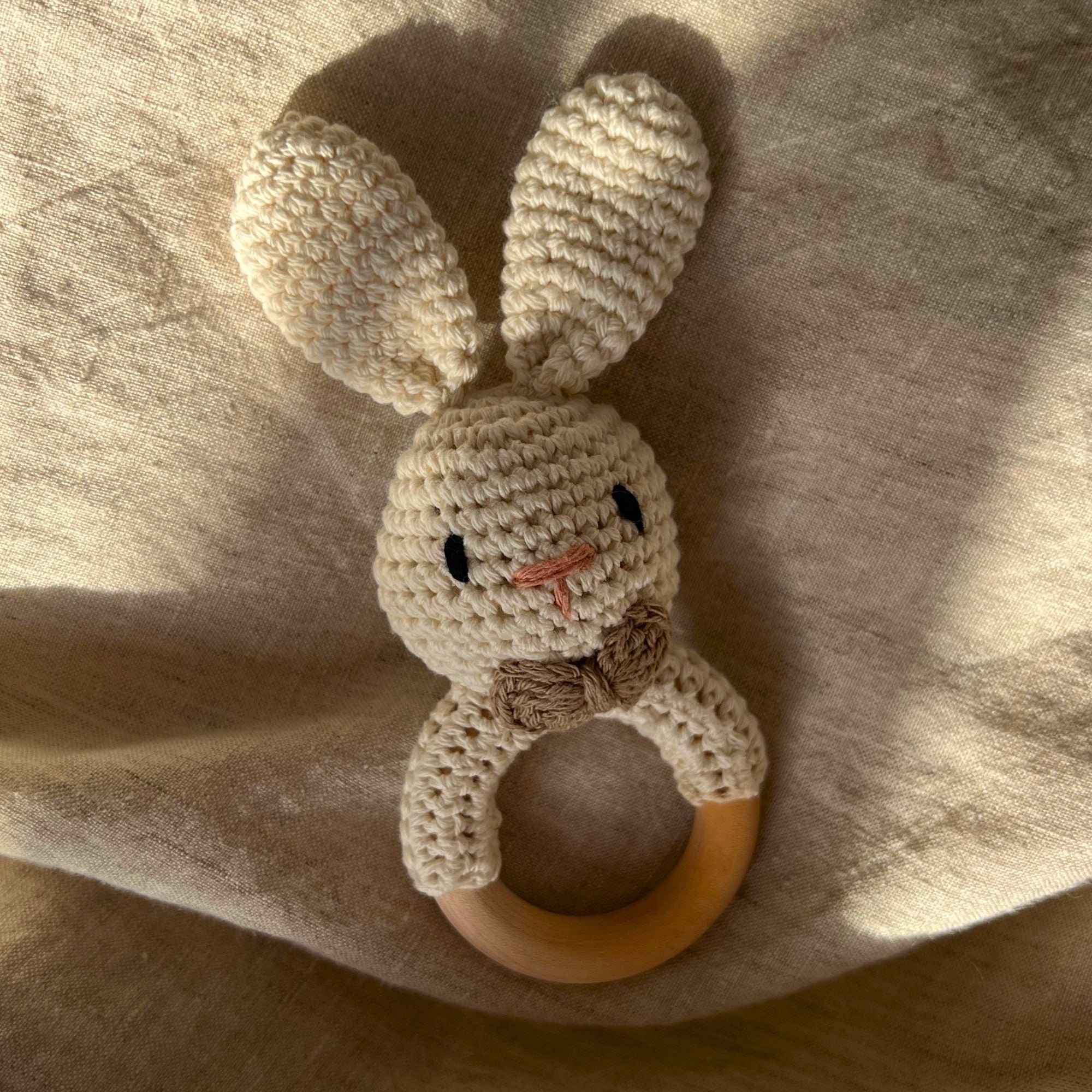 Knitted bunny rattle with wooden ring on a soft fabric background