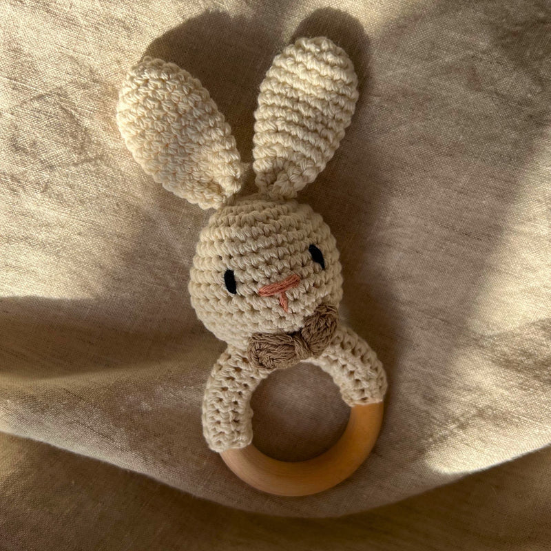 Knitted bunny rattle with wooden ring on a soft fabric background