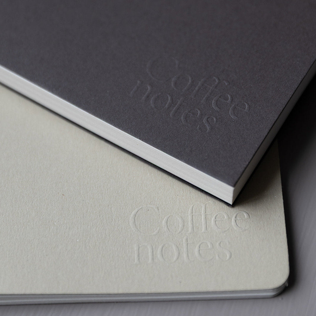 Two notebooks with 'Coffee notes' embossed on their covers, one gray and one beige.