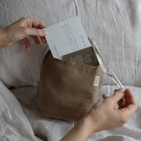 Person opening a brown fabric pouch with a card inside on a soft surface.