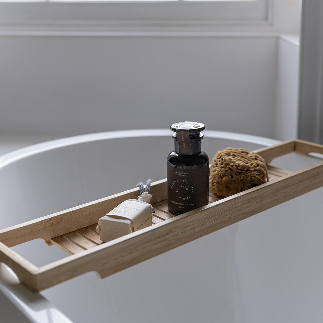 Bathroom setup with a wooden bath tray holding a bottle, soap, and loofah on a bathtub.
