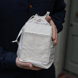 Person holding a white drawstring bag with a pocket against a neutral background
