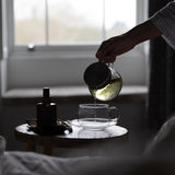 Person pouring tea from a teapot into a cup on a small table.