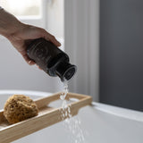 a person pouring Quiet Hours Magnesium Muscle Soak into the bath.